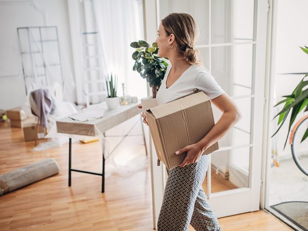 pricing Woman holding box in room filled with moving and household items.